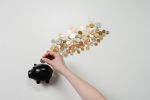 A imagem mostra uma pessoa colocando moedas em um cofre em forma de porquinho. Ela ilustra a matéria que fala sobre Tesouro Direto.