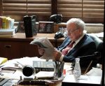 A imagem mostra um senhor lendo um jornal, sentado em uma cadeira de escritório. Na mesa em sua frente, há um livro de Ben S. Bernank, ex-presidente da Reserva Federal, o banco central dos Estados Unidos.