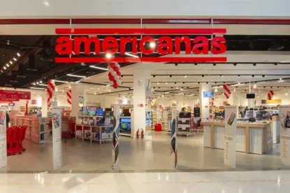 Entrada de ampla loja da Americanas (AMER3) com o banner da marca no teto e bancadas de produtos ao fundo.