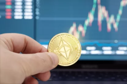 Imagem mostra moeda que simboliza o ethereum entre os dedos de uma mão.