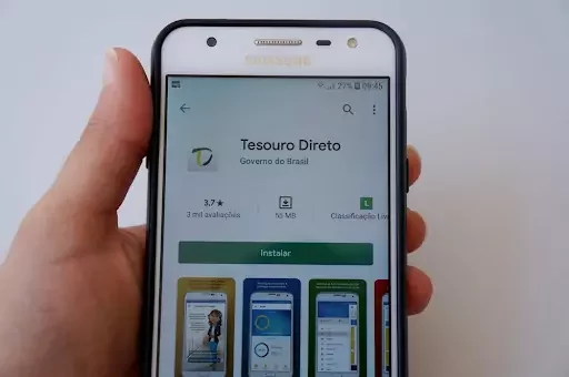 Mão segura smartphone com aplicativo do Tesouro Direto aberto