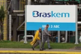 Imagem mostra funcionários equipados com itens de EPI caminhando em frente a placa da Braskem.