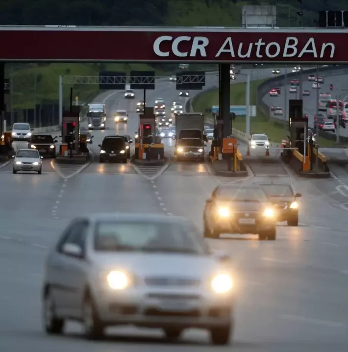 Imagem mostra saída de pedágio da CCR em rodovia, com movimento de veículos.