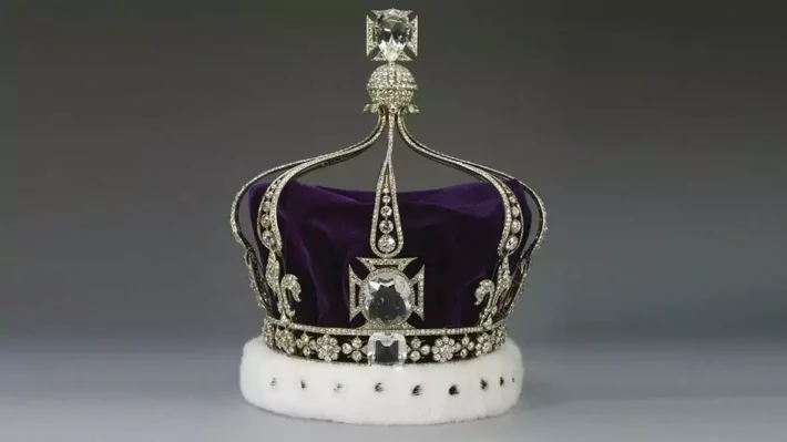 Fundo branco com coroa no centro. A coroa tem um tecido roxo e uma armação de metal prateado cravejado em pedras preciosas.