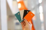 Mão segura um leque de cartões de crédito coloridos.