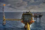 plataforma de petróleo em oceano aberto, com chaminé com chama na ponta.