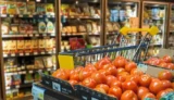Gôndola com tomates à frente de carrinhos de compras e prateleiras refrigeradas cheias de produtos