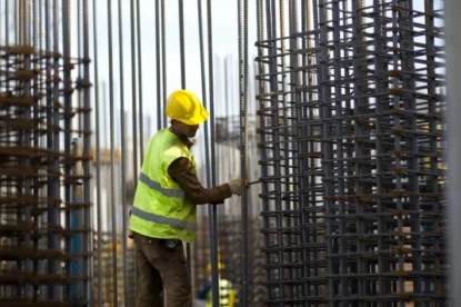 Trabalhador da construção civil trabalha em estrutura de prédio vestindo colete e capacete de obra