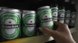 Mão retira uma das latas da cerveja Heineken dispostas em uma prateleira