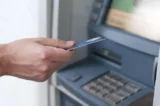 Mão segura cartão de banco para insercao manual no caixa eletrônico.