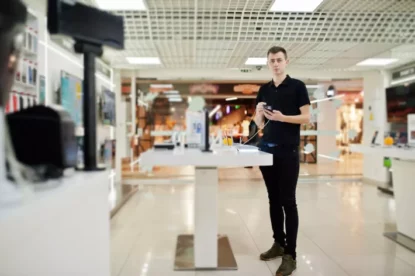 Jovem vendedor de celular na loja de tecnologia com novo smartphone na mão.