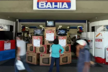 Mulher observa televisores em exposição na fachada da loja.