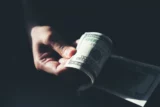 Imagem mostra uma pessoa com dólares na mão.