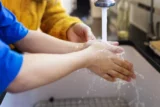 Criança lava as mãos em torneira.