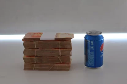 Bolo de notas de dinheiro empilhados com uma lata de refrigerante ao lado para efeito de comparação de altura.