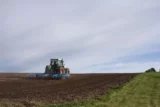 Imagem mostra trator em campo durante preparação da terra para plantio.