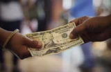 Imagem mostra duas mãos no ato de troca de notas de dólares entre elas.