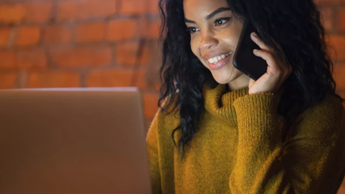 Mulher trabalha em seu laptop enquanto fala ao telefone.