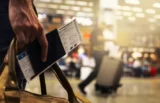 Imagem de bilhete de embarque e passaporte na mão de viajante, dentro de aeroporto.