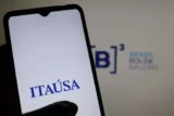 Imagem mostra celular com a logo da Itaúsa na tela.