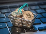 Imagem mostra miniatura de cesta de supermercado com moedas representando o bitcoin dentro.