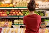 Jovem mulher olha para a colorida prateleira de frutas no supermercado.