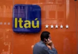 Imagem mostra homem falando no celular enquanto passa em frente a painel com logo do Itaú.