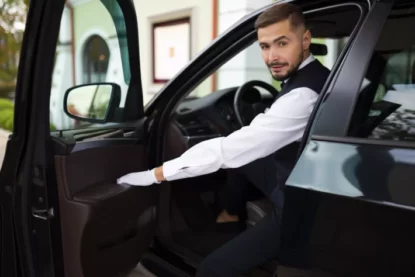 Jovem motorista uniformizado abre porta do carro.