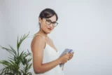 Imagem mostra jovem mulher, de óculos, segurando um caderno e olhando para a câmera.
