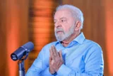 Imagem mostra o presidente Lula, de camisa azul, durante fala ao microfone.