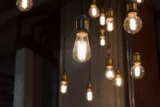 Imagem mostra diversas lâmpadas iluminadas penduradas sob fundo escuro.