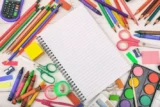 Imagem mostra caderno rodeado por outros materiais escolares coloridos, como lápis, tesoura e borracha.