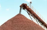 Imagem mostra esteira despejando minério-de-ferro em uma pilha da commodity ao ar livre.