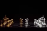 Imagem mostra peças de cavalos rivais do jogo de xadrez no centro do tabuleiro, escorados pelas restantes atrás.