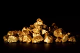 Imagem mostra pepitas de ouro sobre fundo negro.