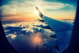 Imagem mostra vista das núvens e do Sol pela janela de um avião.