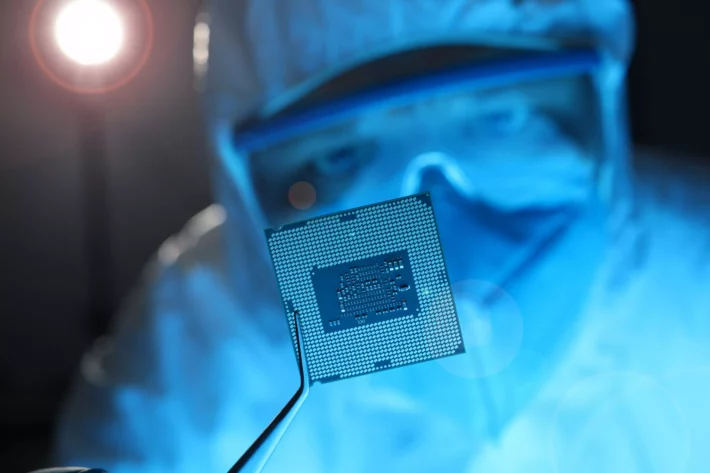 Imagem mostra técnico com equipamento de esterilização segurando chip de computador com uma pinça.