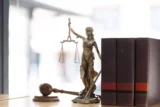 Imagem mostra pequena estátua em cima de mesa que simboliza a Justiça com uma balança nas mãos.