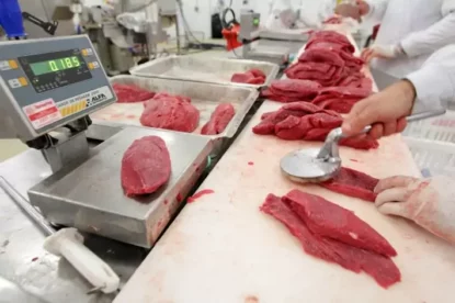 Imagem mostra linha de produção de carnes, com funcionários cortando peças de carne.