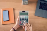 Mulher segurando e pressionando calculadora para calcular despesas de renda e planos para gastar dinheiro no escritório doméstico.