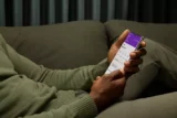 Imagem mostra detalhe de homem no sofá vendo aplicativo do Nubank no celular.