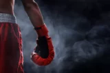 Foto mostra detalhe da luva direita de lutador de boxe sob névoa.