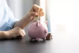 Imagem mostra jovem colocando moeda em cofre de porquinho.