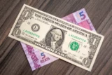 Imagem mostra nota de 1 dólar sobre nota de 5 reais.