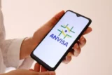 Mão segurando celular com a logo da Anvisa na tela