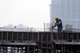 Imagem mostra operário trabalhando na laje de edifício.