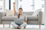 Mulher vencedora, laptop e punho no alto em comemoração pelo sucesso no mercado de ações. Mulher, computador e feliz na sala de casa.