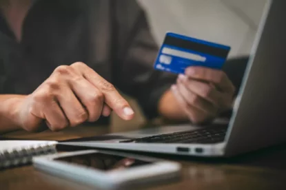 Homem segura cartão em frente a um computador e um celular