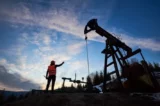 Imagem mostra trabalhador de petroleira em frente a poço de extração em terra.