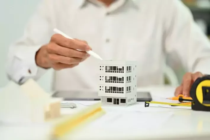 Foto aproximada de um arquiteto trabalhando com um modelo arquitetônico residencial na mesa do escritório.